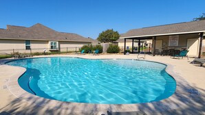A swimming pool with a curved edge, surrounded by lounge chairs and a covered area with tables. - 2BR Townhome • EV Charger • Near Texas A&M (College Station)
