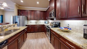 A modern kitchen with dark wood cabinets, granite countertops, stainless steel appliances, and a tiled backsplash. - 2BR Townhome • EV Charger • Near Texas A&M (College Station)