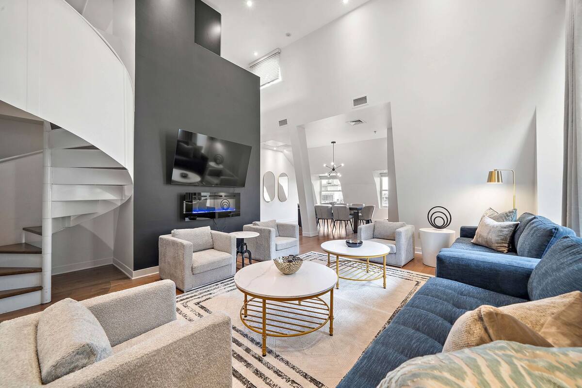 A modern living room with a spiral staircase, a flat-screen TV, and a dining area with a chandelier.