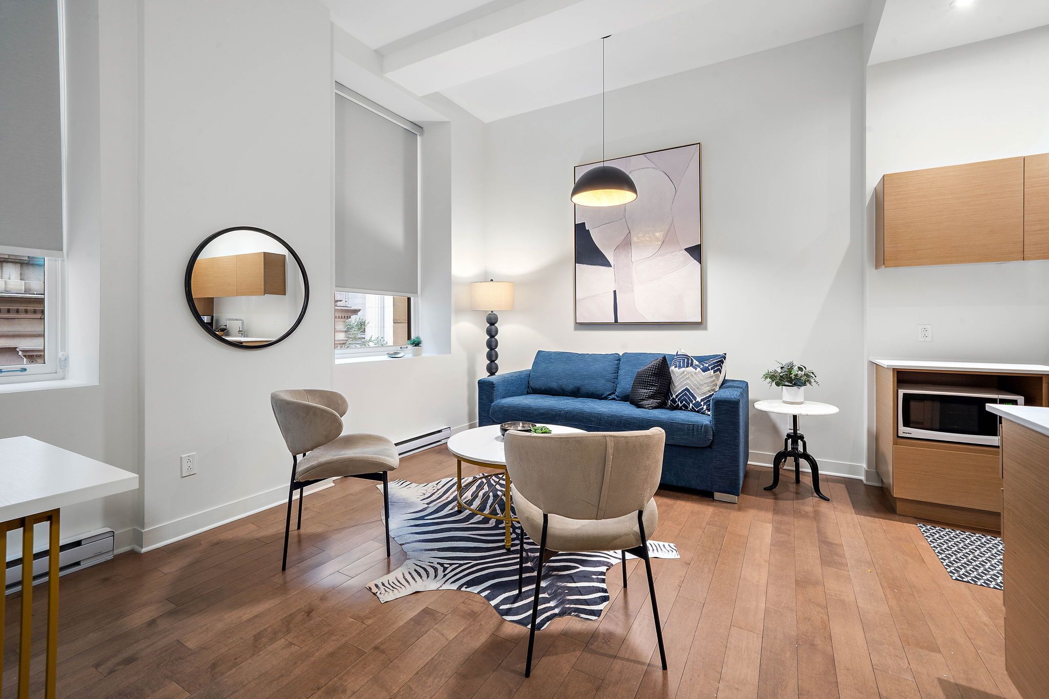 A modern living room with a blue sofa, two armchairs, a round coffee table, a zebra rug, and a contemporary art piece.