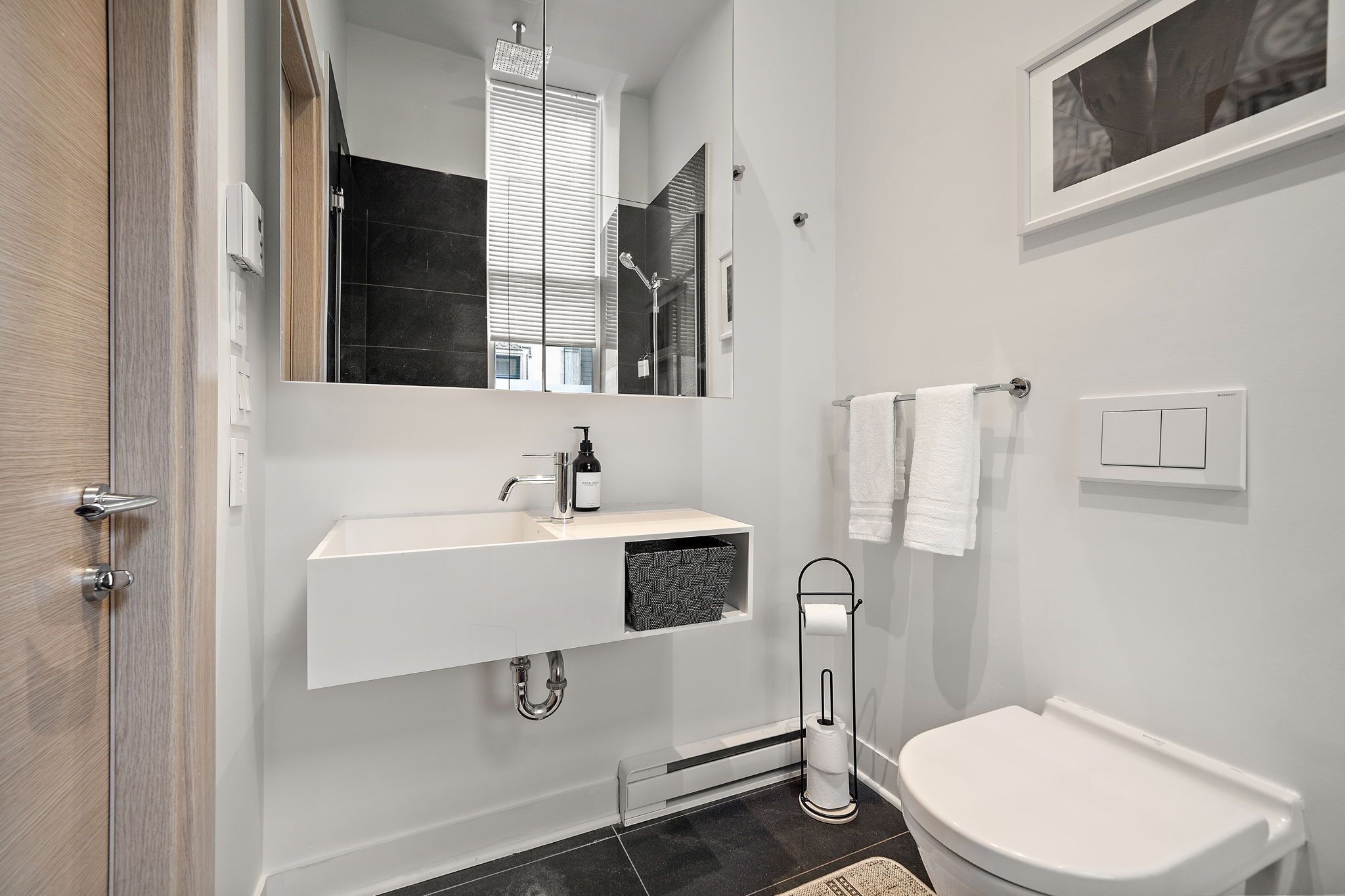 A modern bathroom with a white sink, a mirror, a toilet, and a towel rack.
