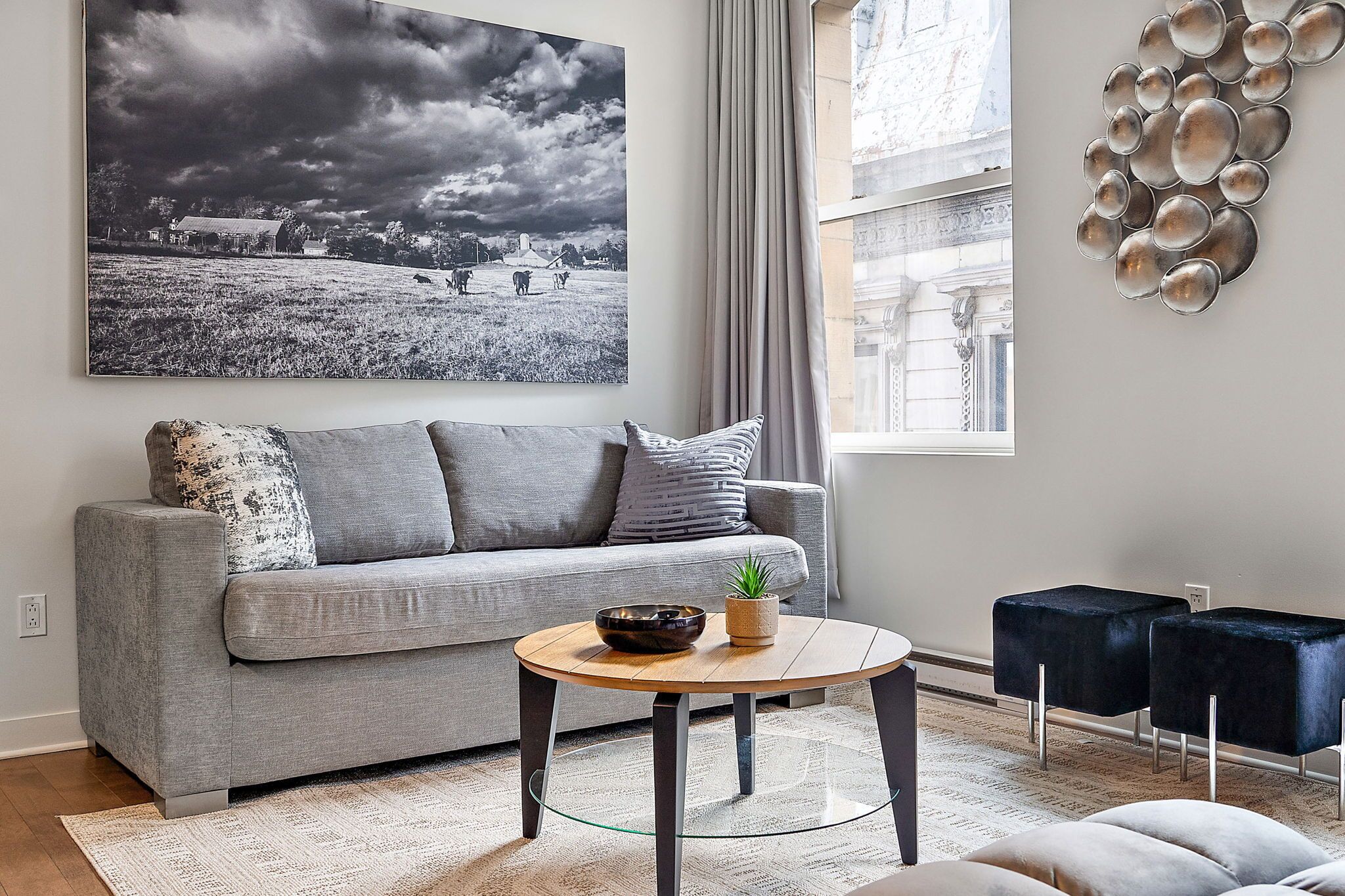 A modern living room with a grey sofa, a round coffee table, and a black and white landscape painting.