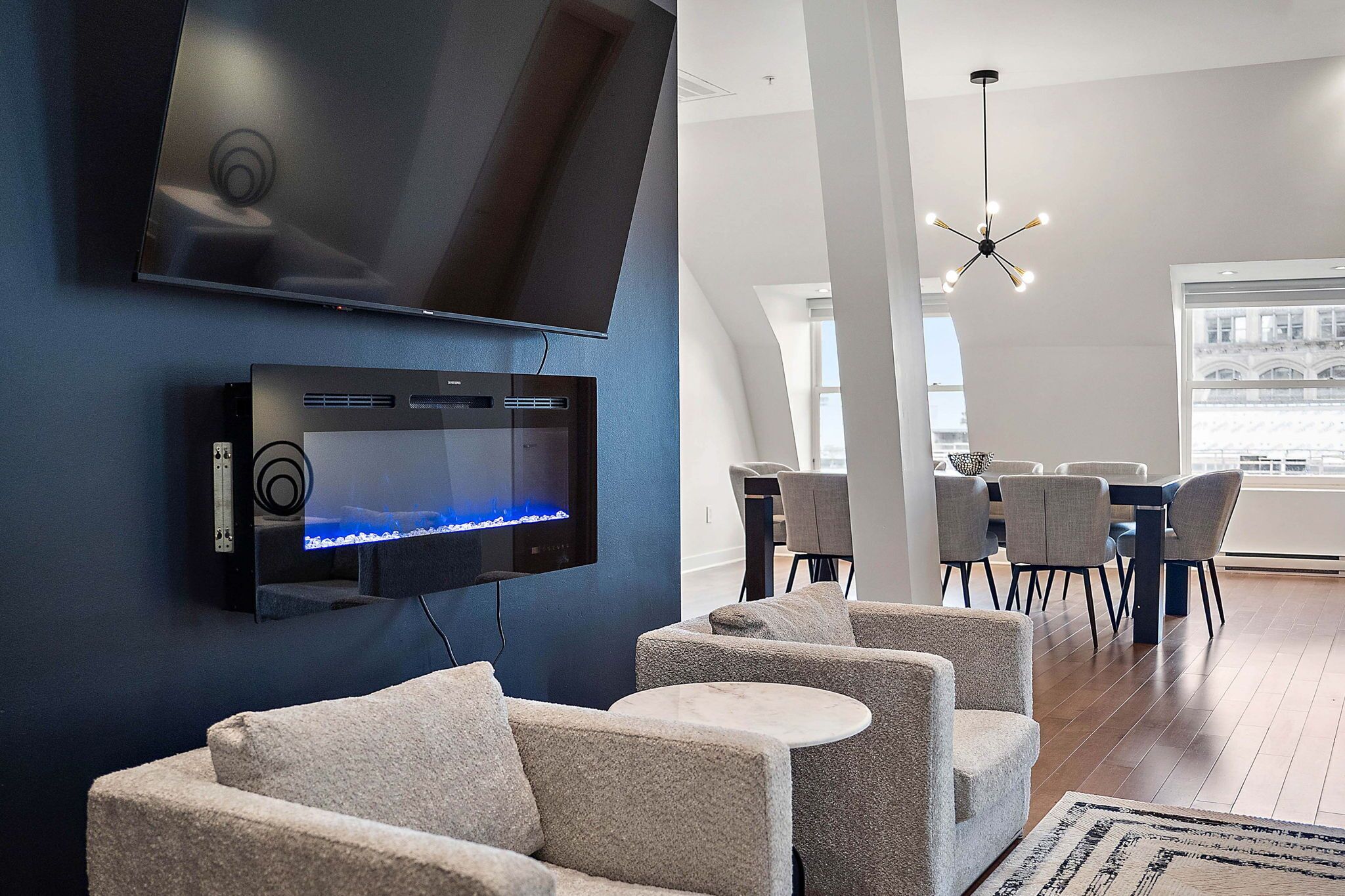 A modern living room with a flat-screen TV, a sound system, and a dining area with chairs and a table.