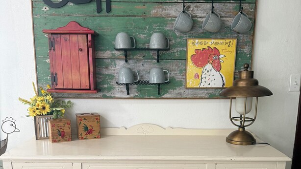 A white dresser with three drawers, a vintage lamp, and a wall-mounted coffee-themed decoration.