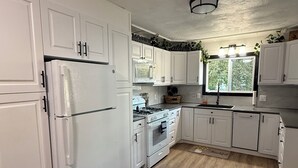A kitchen with white cabinets, a refrigerator, stove, and sink.