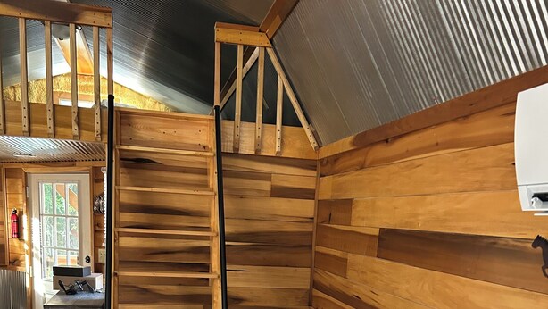 Ein gemütliches Wohnmobil-Interieur mit Holzvertäfelung, einer grauen Couch, einem Holztisch und einer Treppe zu einem Schlafbereich oben.