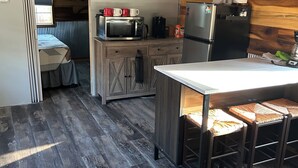 Eine kleine Küche mit Mikrowelle, Kaffeemaschine und Kühlschrank. Ein Holztisch mit Stühlen steht bereit.