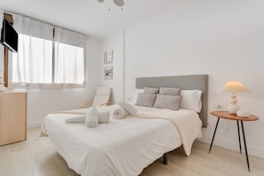 A bedroom with a bed, a bedside table, a chair, a lamp, and a TV on a stand.