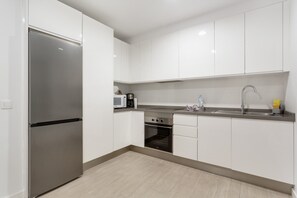 Une cuisine moderne avec des armoires blanches, un réfrigérateur en acier inoxydable, un four à micro-ondes, un évier et une cuisinière.