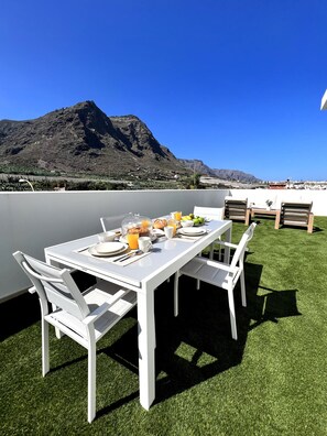 Une table blanche dressée à l’extérieur, avec vue sur la montagne, entourée de chaises blanches.