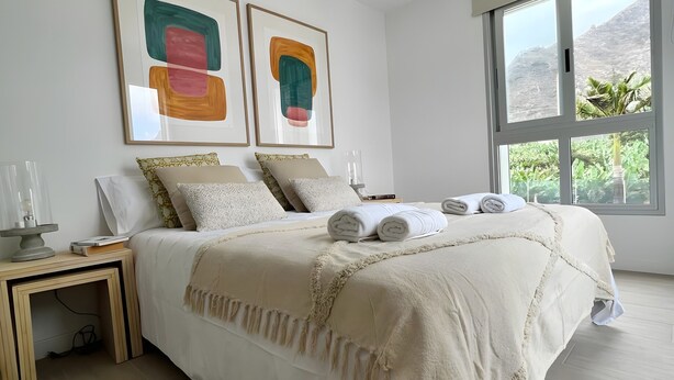 Un dormitorio con cama, mesitas de noche, una ventana con vistas y arte abstracto en la pared.