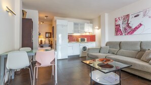 A modern living room with a sofa, a glass coffee table, and a dining area with chairs. - Exclusive Beachfront Apartment. (Costa Adeje)