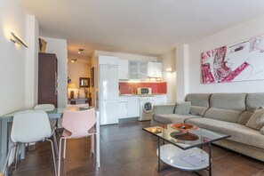 A modern living room with a sofa, a glass coffee table, and a dining area with chairs.