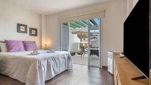 A bedroom with a bed, a TV, and a balcony with a table and chairs. - Exclusive Beachfront Apartment. (Costa Adeje)
