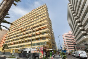A multi-story hotel with balconies, a visible ground floor with shops, and a clear sky.