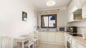 Eine Küche mit Esstisch, Stühlen, einer Mikrowelle, einer Kaffeemaschine und einem Fenster mit Vorhängen.