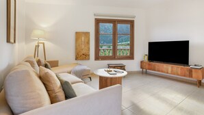 Ein Wohnzimmer mit einer Couch, einem Couchtisch, einem Fernseher, einer Lampe und einem Fenster mit Blick.
