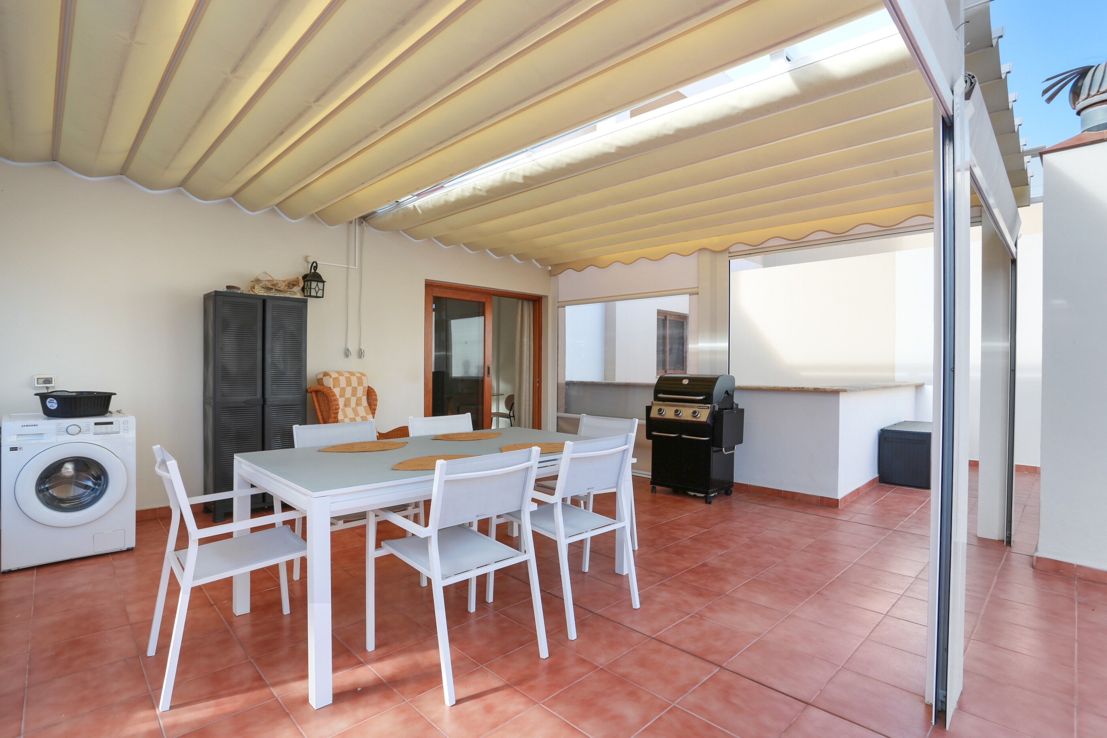 Un comedor con mesa y sillas, lavadora, parilla y ventana.
