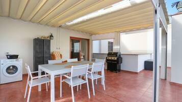 Un comedor con mesa y sillas, lavadora, parilla y ventana.