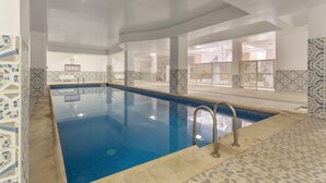 A swimming pool with clear blue water, surrounded by patterned tiles and columns.