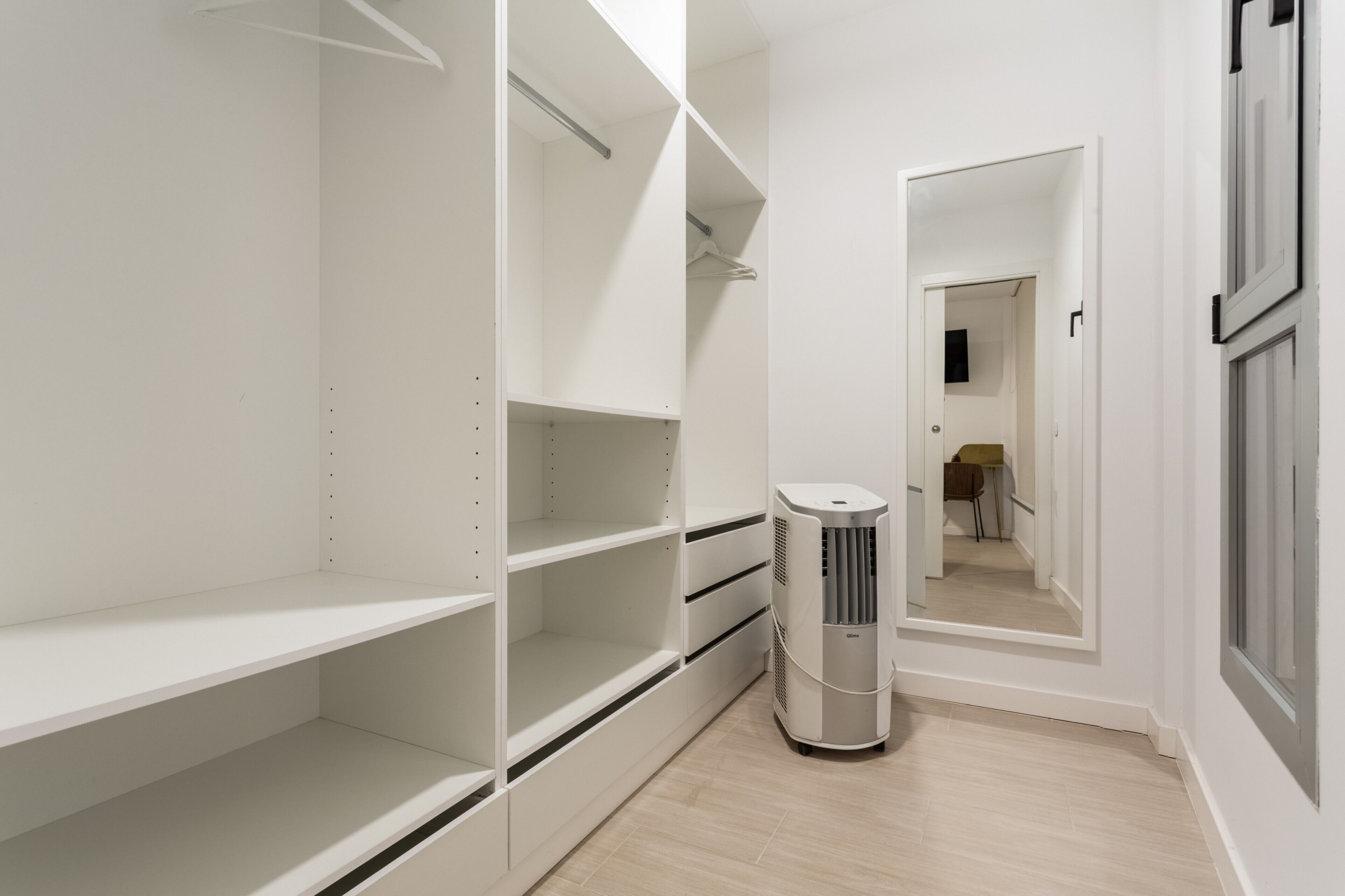 Een inloopkast met open planken, een spiegel en een staande verwarming.
