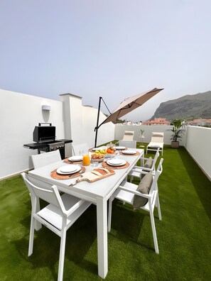 A rooftop terrace with a dining table set for four, a grill, and a large umbrella. - Vacation Apartment 'Apto Moderno Con Vistas Únicas' with Sea View, Private Terrace and Wi-Fi (Los Silos)