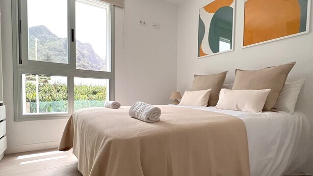 Ein Schlafzimmer mit Bett, Fenster und abstrakten Wandbildern.