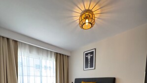 Ein Hotelzimmer mit Bett, Nachttisch, Wandlampe, Vorhängen am Fenster und einem gerahmten Bild an der Wand.