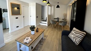 Ein modernes Wohnzimmer mit einem Holztisch, einem grauen Sofa und einem Essbereich mit Glastisch und Stühlen.