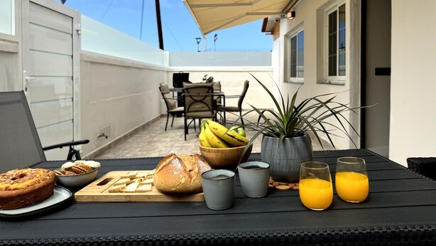 Ein Essbereich mit Tisch, gedeckt für das Frühstück, inklusive Brot, einer Pflanze und Gläsern Orangensaft.