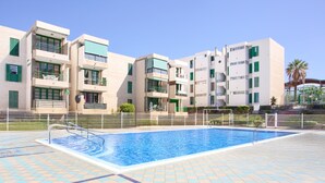 A swimming pool with tiled flooring, surrounded by a fence, and adjacent to a multi-story building with balconies.