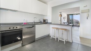 A modern kitchen with stainless steel appliances, white cabinetry, and a bar area with stools.