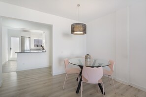 A modern kitchen with a stainless steel refrigerator, a glass island, and a hanging pendant light.