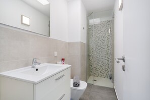 A modern bathroom with a white sink, a glass shower enclosure, and a toilet.