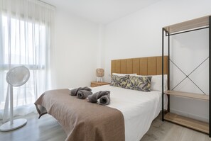 A hotel room with a bed, a bedside table, a fan, and a window with curtains.