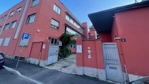 A red building with a parking sign, a gated entrance, and a staircase leading to the entrance. - Flora: 1 Bedroom Apartment 1 (Milano)