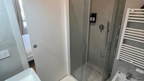 A modern bathroom with a glass-enclosed shower, a white sink, and a towel rack. - Flora: 1 Bedroom Apartment 1 (Milano)