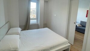A bedroom with a bed, a window with curtains, and a door leading to another room. - Flora: 1 Bedroom Apartment 1 (Milano)
