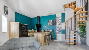 Une cuisine moderne avec un îlot central en bois, un canapé gris et un escalier en colimaçon.