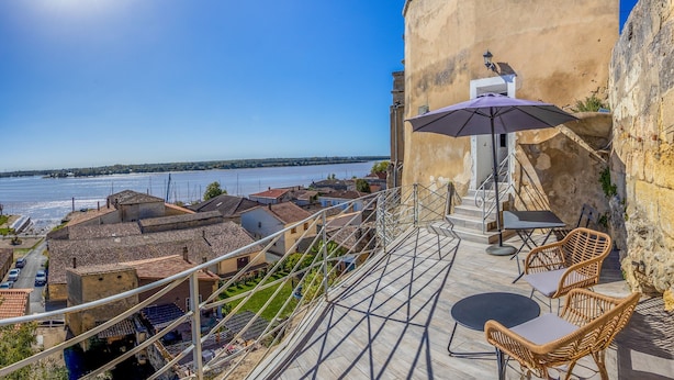 Une terrasse meublée avec des meubles en osier, une vue sur une rivière et un bâtiment à la façade en pierre.