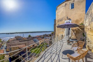 Una terraza con mobiliario de mimbre, vistas a un río y un edificio de fachada de piedra.