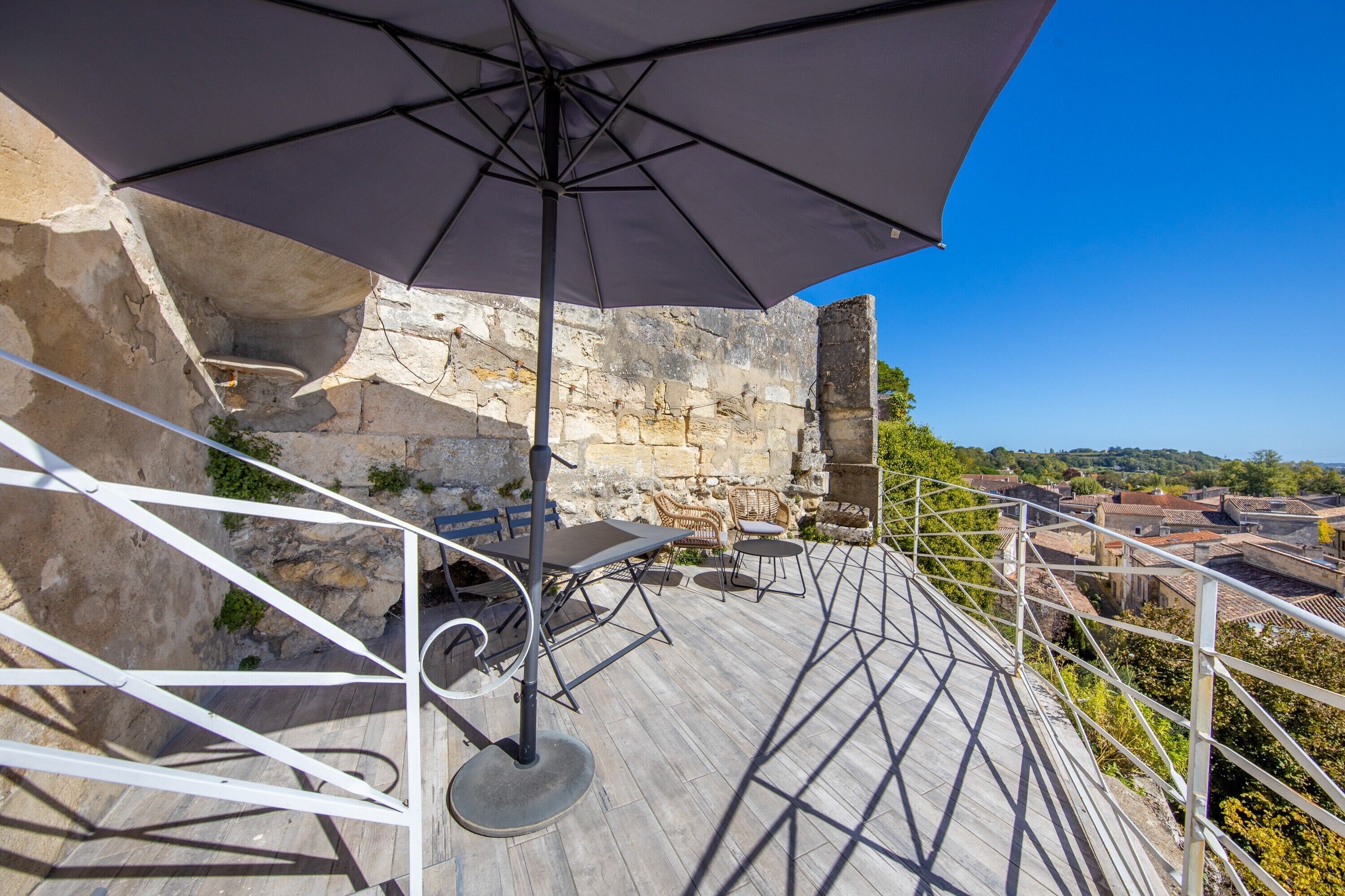 Una terraza con una mesa, sillas y una sombrilla, además de un muro de piedra.