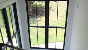 Una escalera de madera con barandales negros que conduce a un rellano con ventanas grandes que dan a un césped.