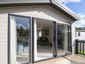 A modern house with a large sliding glass door leading to a living room with a sofa and a dining table. - Altair Lodge (Crieff)