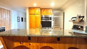 A modern kitchen with wooden cabinets, a granite countertop, stainless steel appliances, and three bar stools. - 1+ bedroom bungalow in Kings Beach with a fully fenced in yard. (Kings Beach)