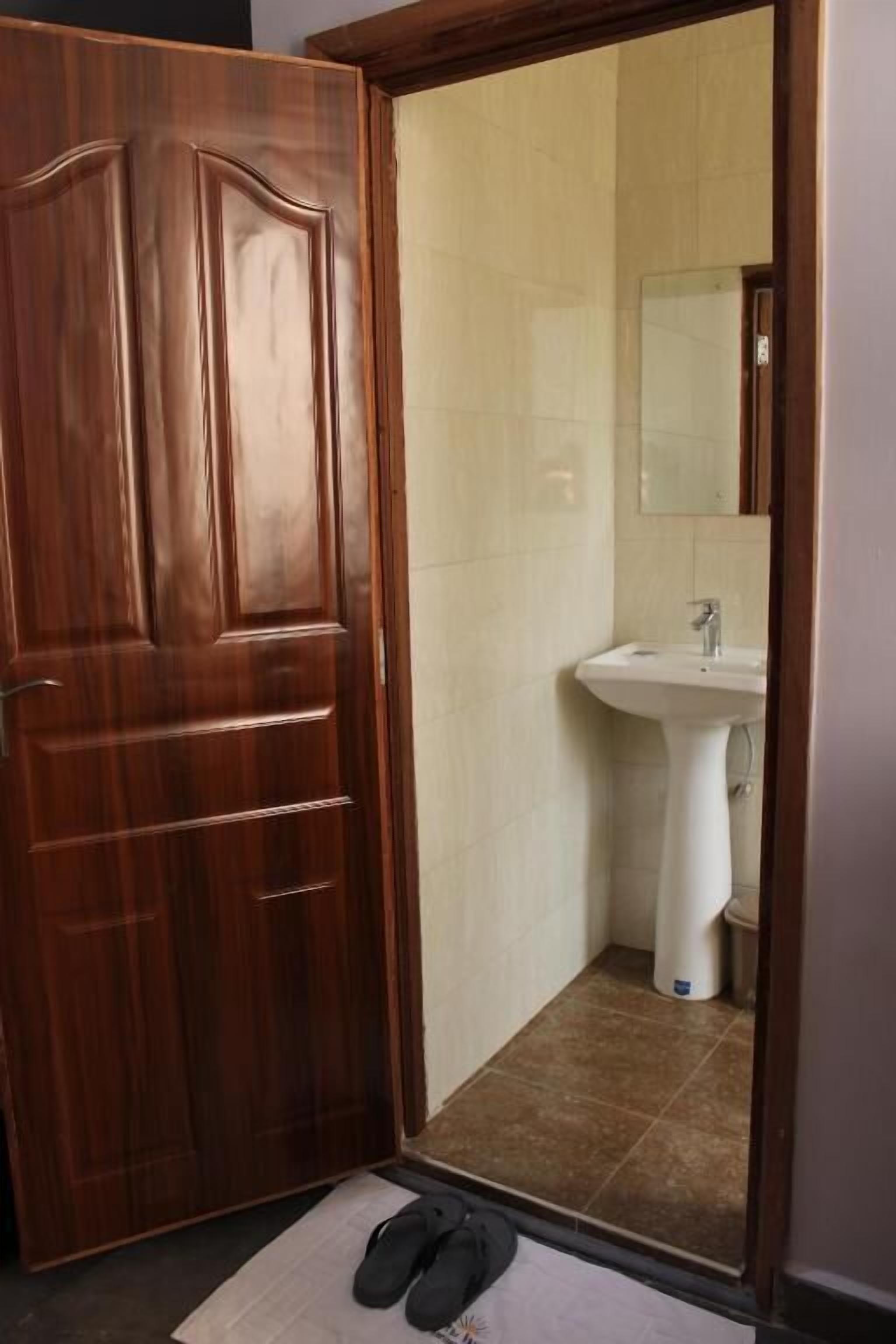 A wooden door leading into a bathroom with a white sink and a mirror above it.