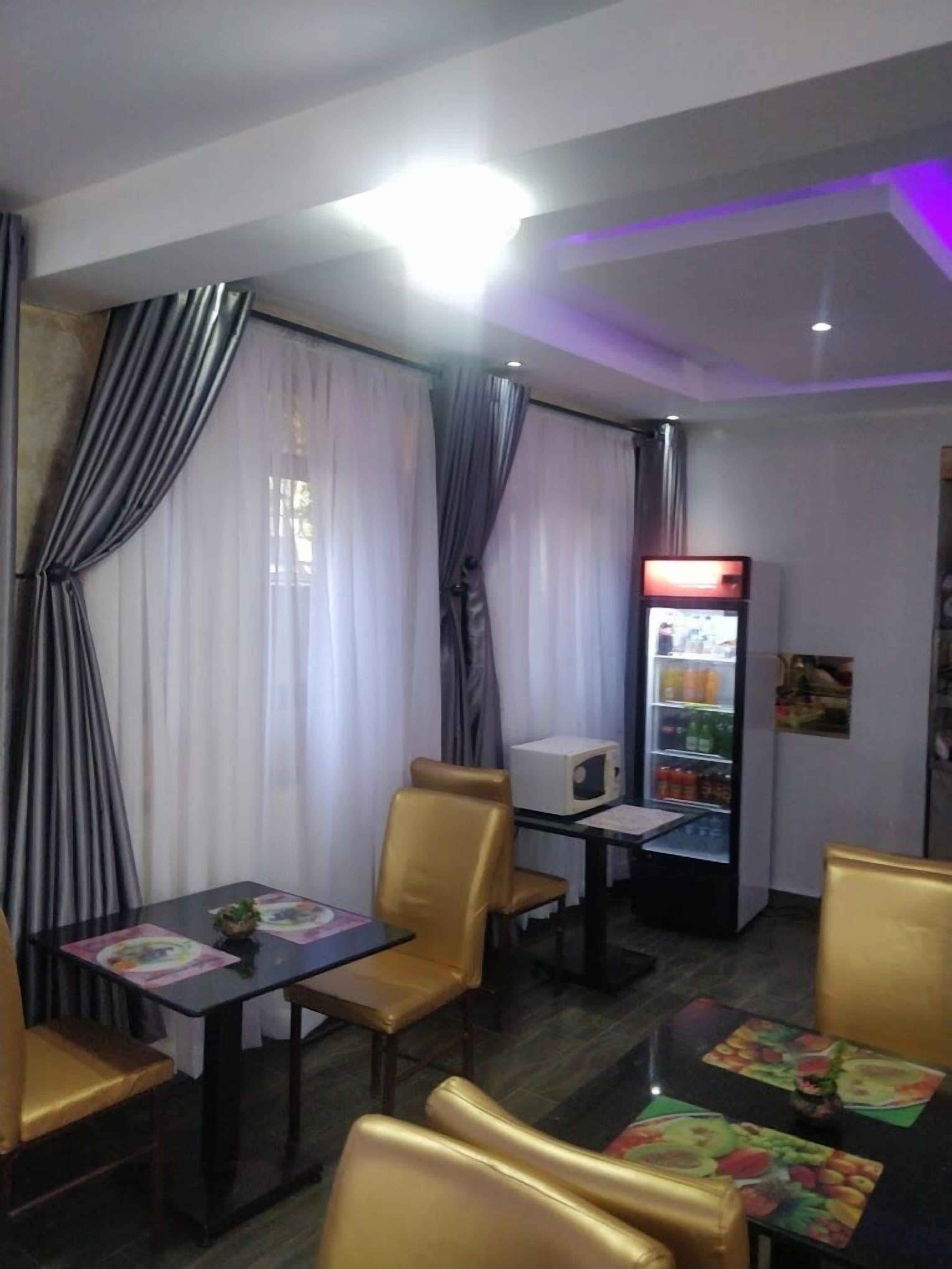 A dining area with tables and chairs, a refrigerator, and curtains.