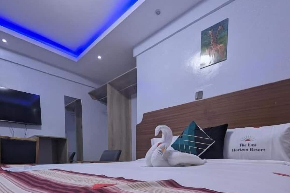 A hotel room with a bed, a flat-screen TV, a wooden headboard, and a painting on the wall.