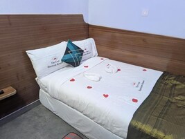 Una cama bien tendida con una colcha blanca adornada con corazones rojos y un logotipo, una almohada con un logotipo y un cabecero de madera.