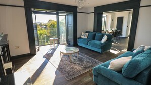 Ein geräumiger Wohnbereich mit großem Fenster, einem blauen Sofa, einem Couchtisch und einer Kronleuchter.